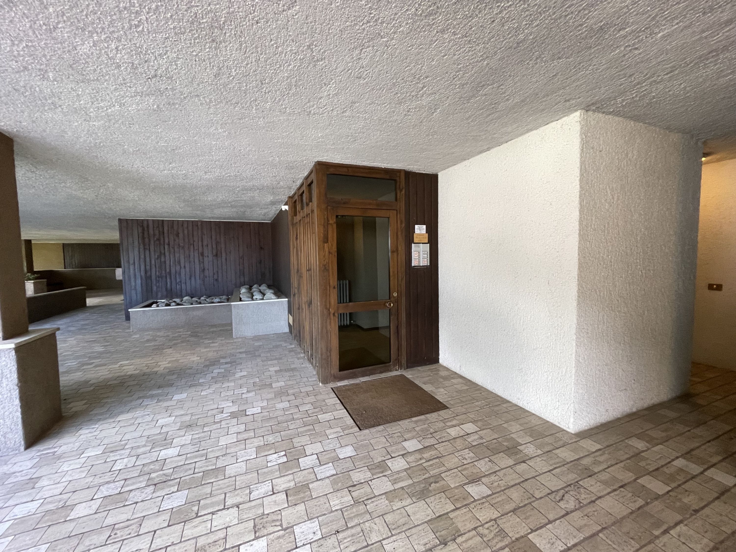 Un'ampia area interna con pavimento a motivi a spina di pesce, una porta in legno e una parete bianca con texture.