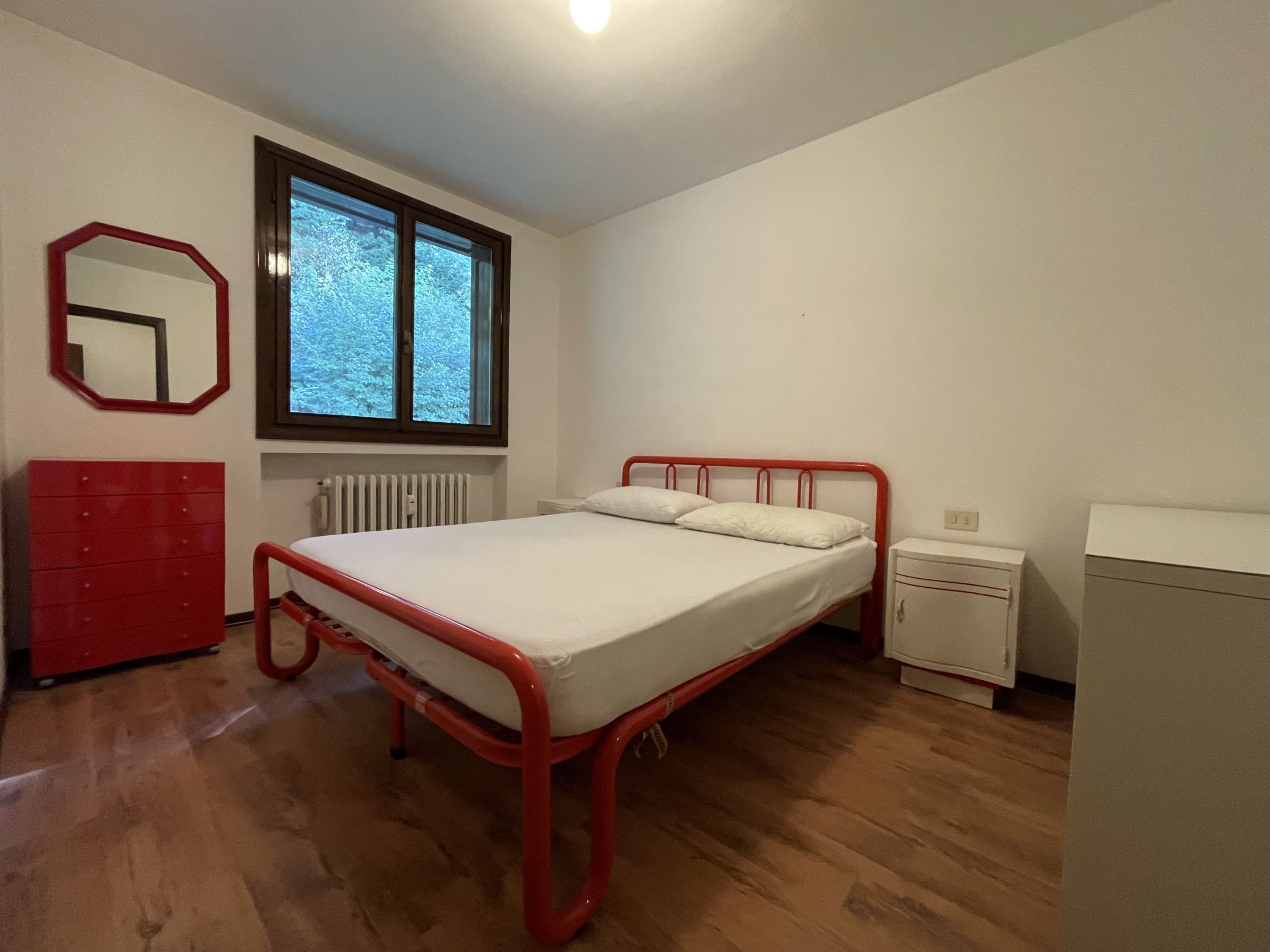 Un dormitorio con una cama individual, un tocador, una mesita de noche, un espejo y una ventana.