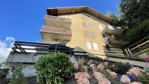 A multi-level building with a yellow facade, wooden balconies, and a stone base.