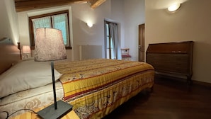 Een slaapkamer met een houten bed, een nachtkastje, een lamp, een dressoir en een raam met gordijnen.