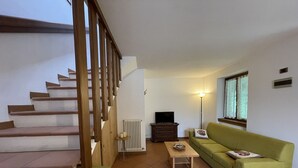 Een woonkamer met een trap, een groene bank, een bijzettafeltje, een radiator en een televisie.