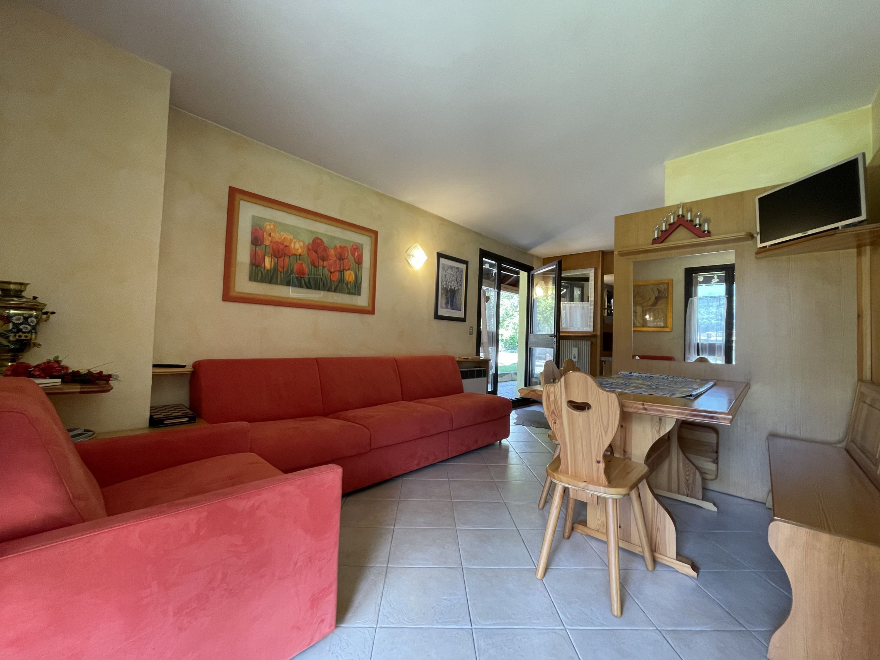Un salon avec un canapé rouge, une table à manger en bois avec une chaise, et un tableau représentant des tulipes accroché au mur.