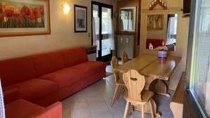 Een eethoek met een houten tafel, vier houten stoelen, een rode bank en een schilderij van tulpen aan de muur.