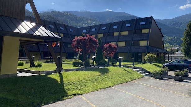 Een hotel met modern design, met een binnentuin en parkeerplaats, omgeven door bergen en groen.