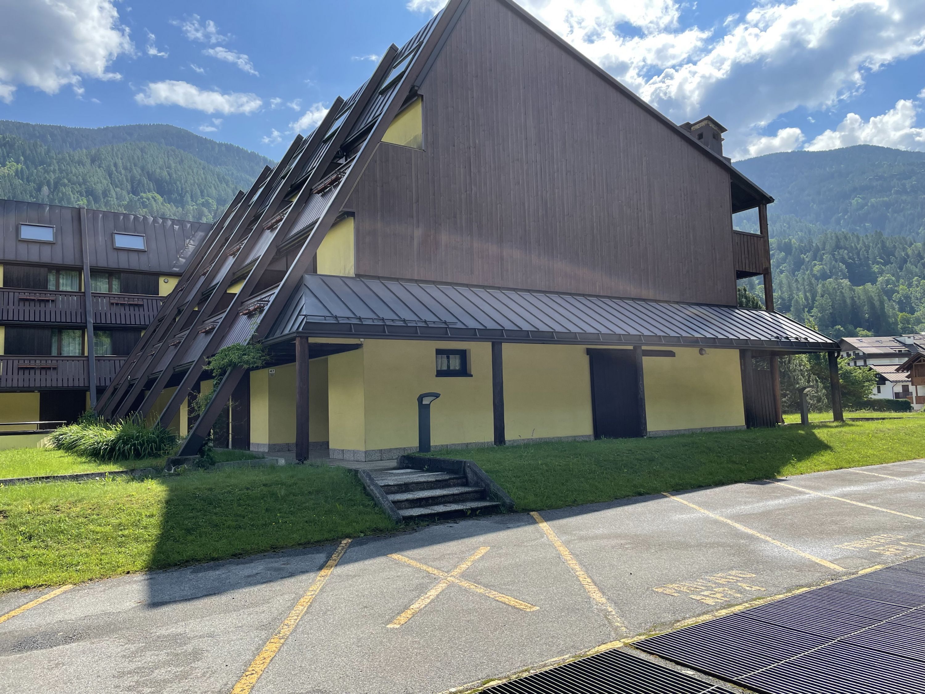 Un edificio con techo inclinado, una escalera que lleva a la entrada y un estacionamiento al frente.