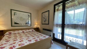 Een slaapkamer met een bed, een stoel, een lamp en twee ingelijste foto’s aan de muur.