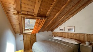 Une chambre avec un plafond en pente, des murs en bois, un lit avec du linge de lit blanc, une table de chevet et deux tableaux encadrés accrochés au mur.