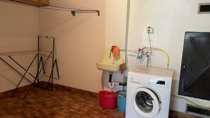 Une buanderie équipée d’un lave-linge, d’un évier, d’un étendoir et d’un seau rouge.