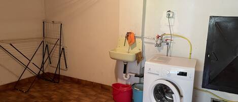 A laundry room with a washing machine, a sink, a drying rack, and a red bucket.