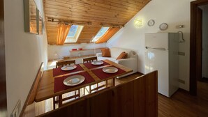 Une cuisine chaleureuse avec un plafond en bois, une table à manger avec des assiettes, un canapé blanc et un réfrigérateur.