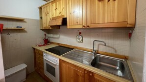 Une cuisine dotée de meubles en bois, d’un évier en acier inoxydable, d’un four encastré et d’un dosseret carrelé.