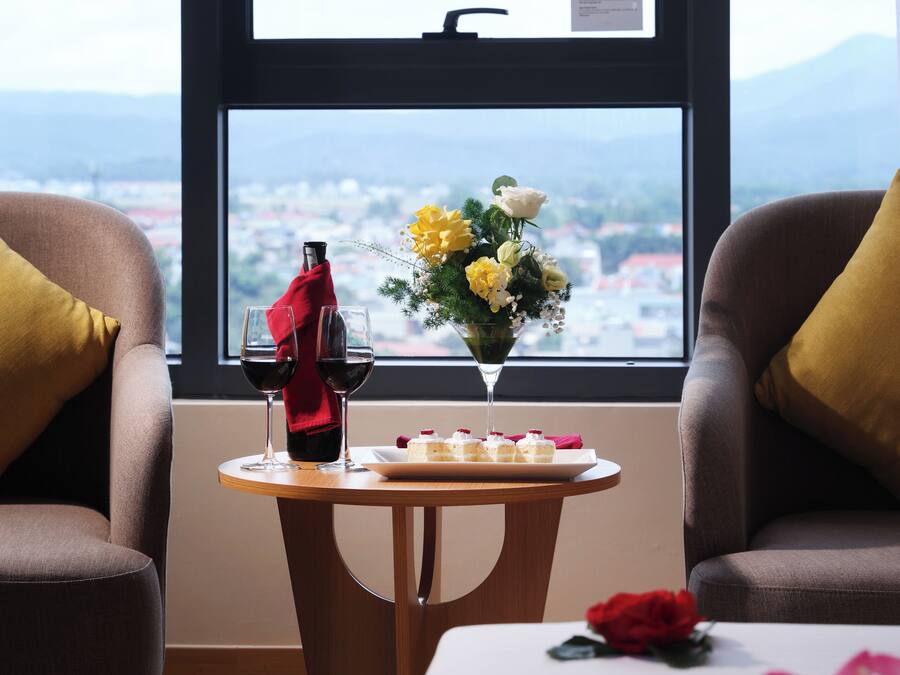 A room with two armchairs, a small round table with a bottle, glasses, and a vase of flowers.