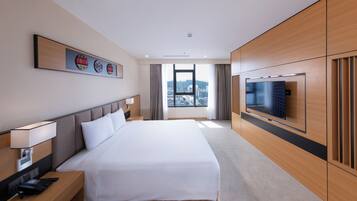 Habitación de hotel con una cama grande, televisor, escritorio con teléfono y ventana con vista a la ciudad.