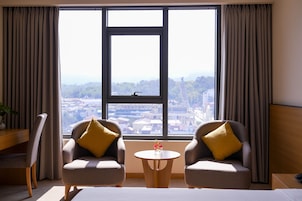 A hotel room with two armchairs, a small round table, and a large window offering a city view.
