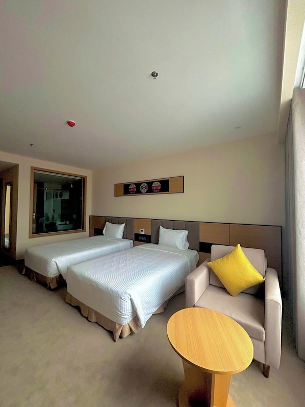 Ein Hotelzimmer mit zwei Betten, einem Sofa, einem kleinen Tisch und einem großen Spiegel.