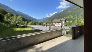Un balcone con vista su un paesaggio montano, una strada e un edificio con tetto rosso.