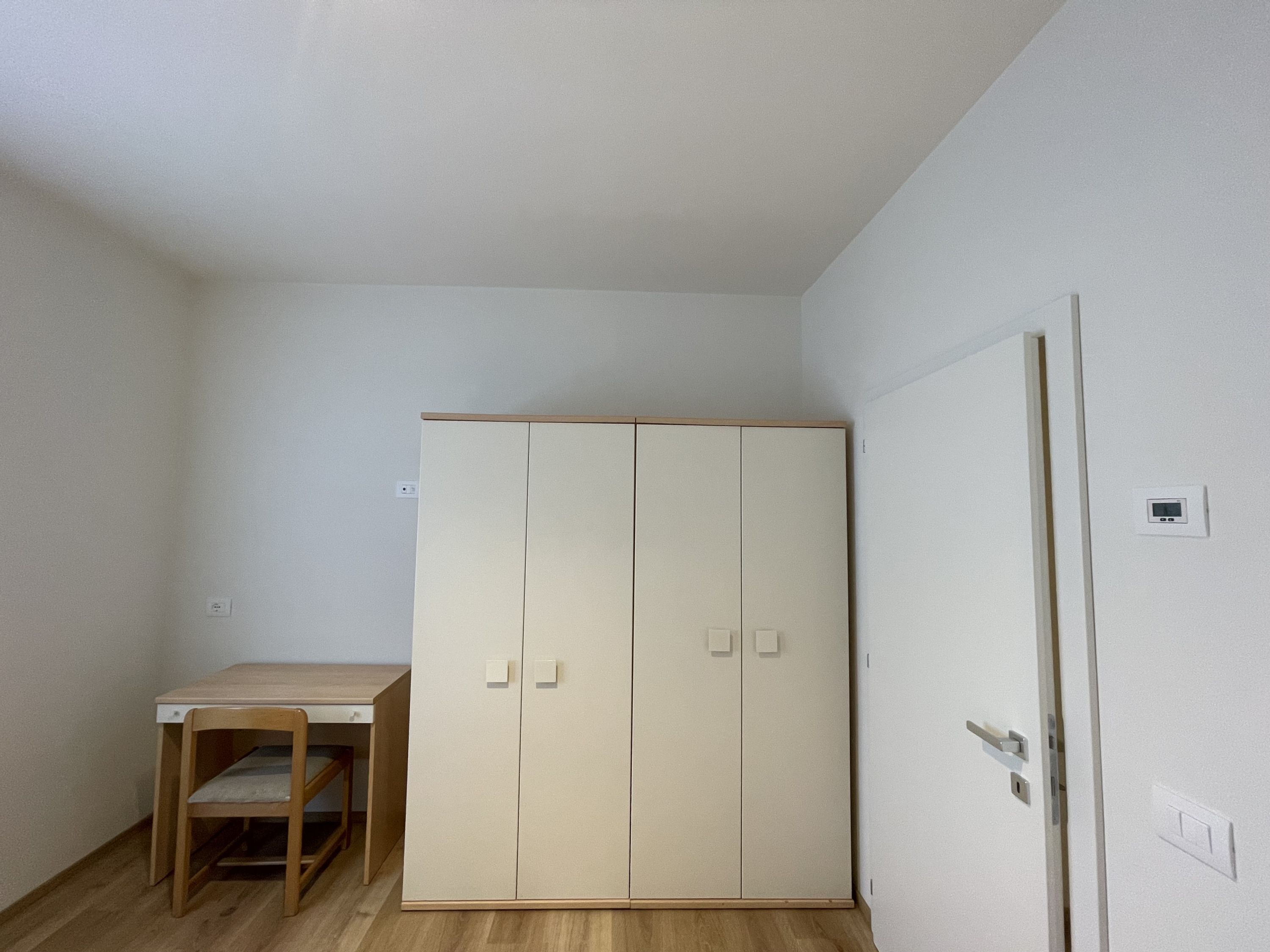 Een kleine kamer met een houten bureau, een kledingkast en een deur.
