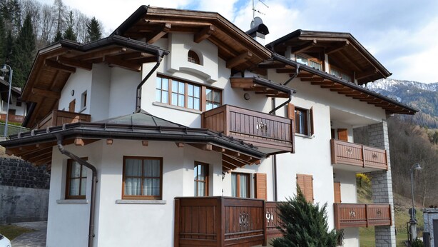 Un chalet a più piani con balconi in legno, gradini in pietra e uno sfondo montuoso.