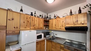 Eine Küche mit Holzausstattung, einem weißen Kühlschrank, einer Mikrowelle, einem Herd und verschiedenen Flaschen in den Regalen.
