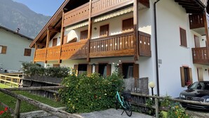 Ein zweistöckiges Holzhaus mit Balkonen, einem Fahrrad und einem Auto vor der Tür.
