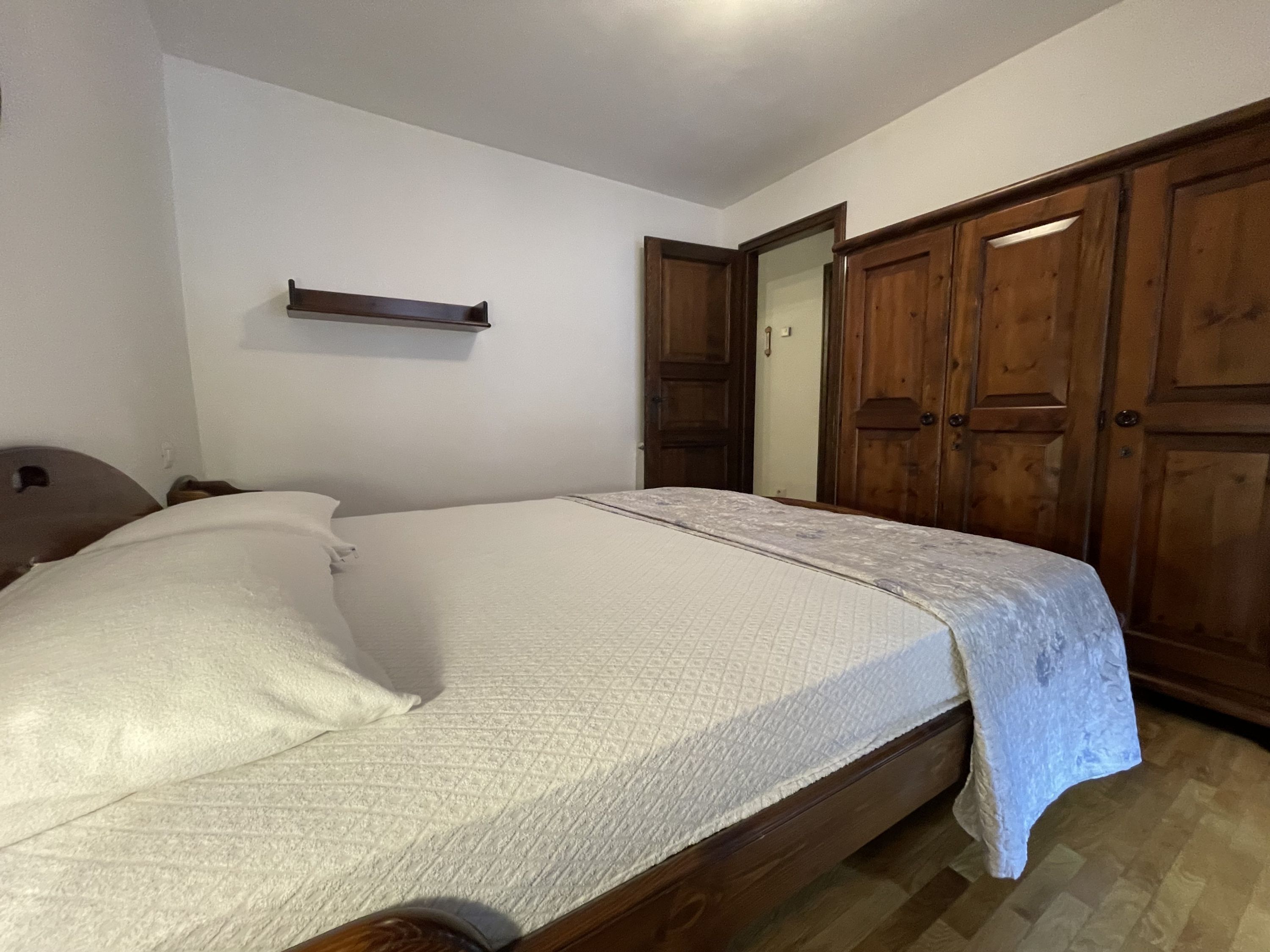Un dormitorio con una cama de madera, un armario de madera y una pequeña estantería sobre la cama.
