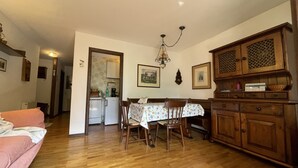 Ein gemütliches Wohnzimmer mit Holzboden, einem rosa Sofa, einem Esstisch mit Stühlen und einer Küchenzeile mit Holzschränken und einem Kühlschrank.