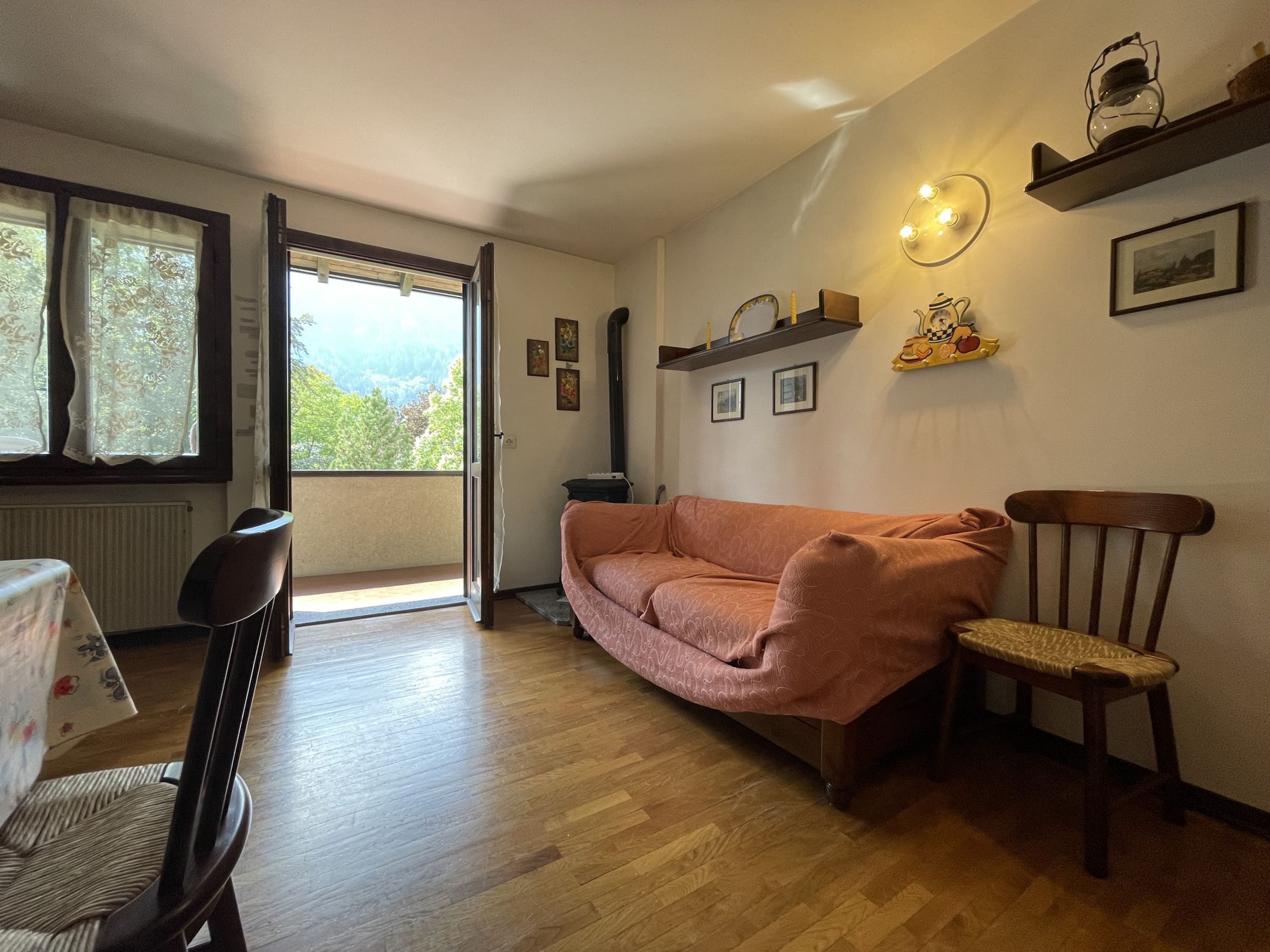 Un salon chaleureux avec un canapé, une chaise en bois, une table et une vue sur l’extérieur par une porte ouverte.