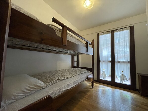 Une chambre avec un lit superposé, une tête de lit en bois, une fenêtre avec des rideaux légers et un plancher en bois.