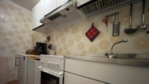 Eine Küche mit Herd, Backofen und Spüle. Ein rotes Tuch hängt an der Wand, und ein Set Küchenutensilien ist vorhanden.