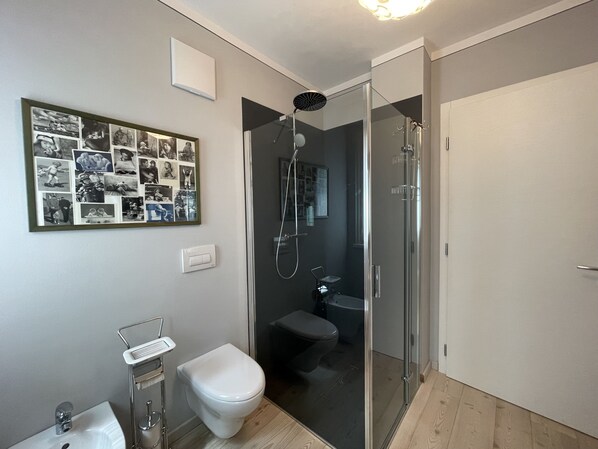 Un baño moderno con ducha de vidrio, inodoro blanco, lavamanos con grifo cromado y una composición de fotos enmarcadas en la pared.