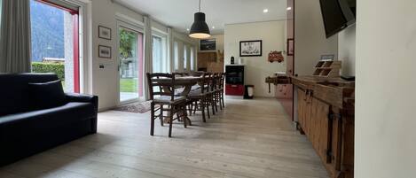 Amplia sala de estar con mesa y sillas de comedor, un sofá negro y una cocina con armarios de madera y televisor.