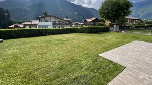 A residential area with houses, a well-maintained lawn, and mountains in the background. - 067 Bilocale Piano Terra Giustino (Giustino)