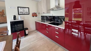 A modern kitchen with red cabinets, a black oven, and a white countertop. There is a framed picture on the wall and a small toy car decoration. - 067 Bilocale Piano Terra Giustino (Giustino)