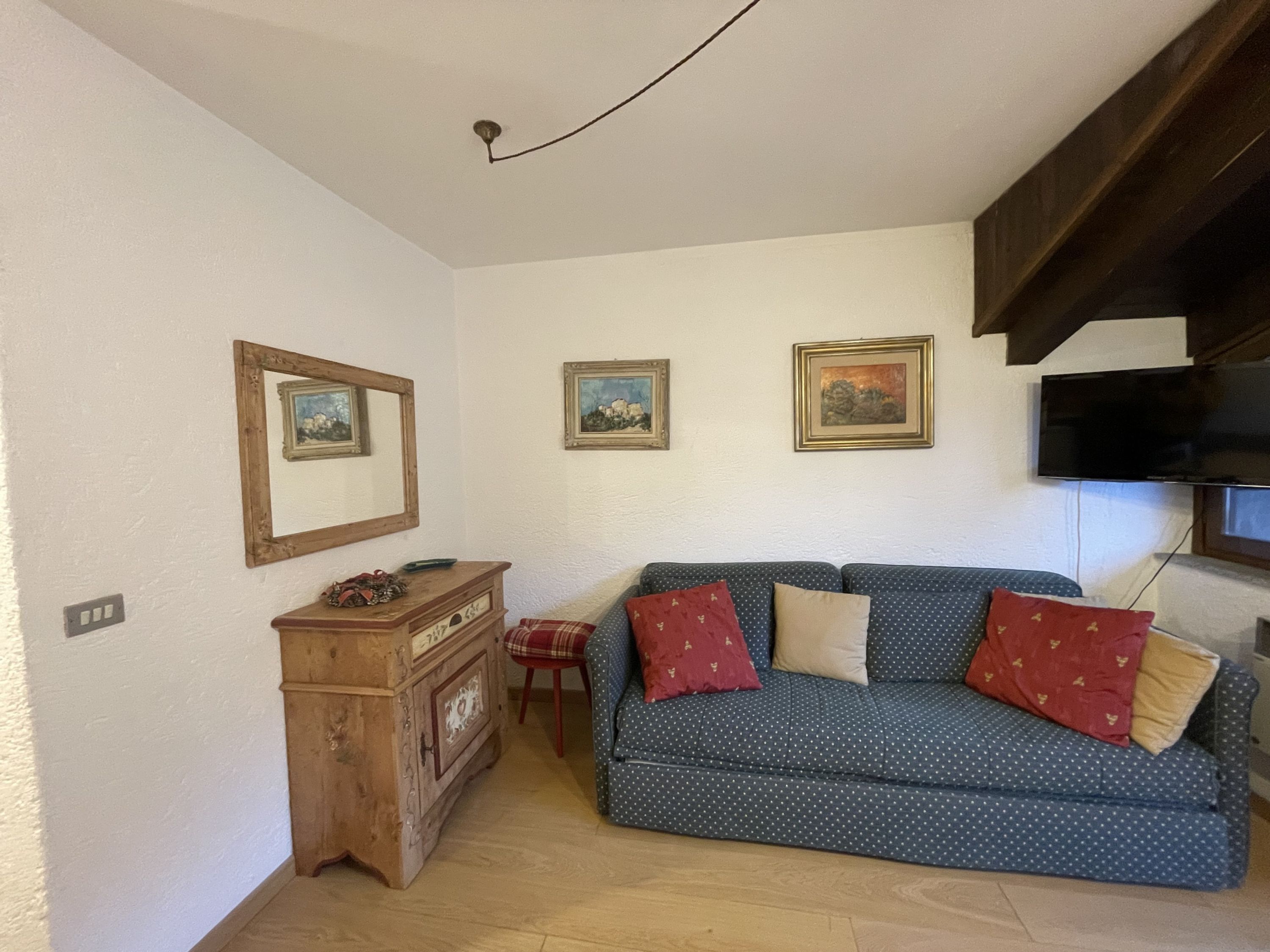 A living room with a dark blue sofa with white polka dots, two red pillows, a wooden cabinet, and three framed pictures on the wall.
