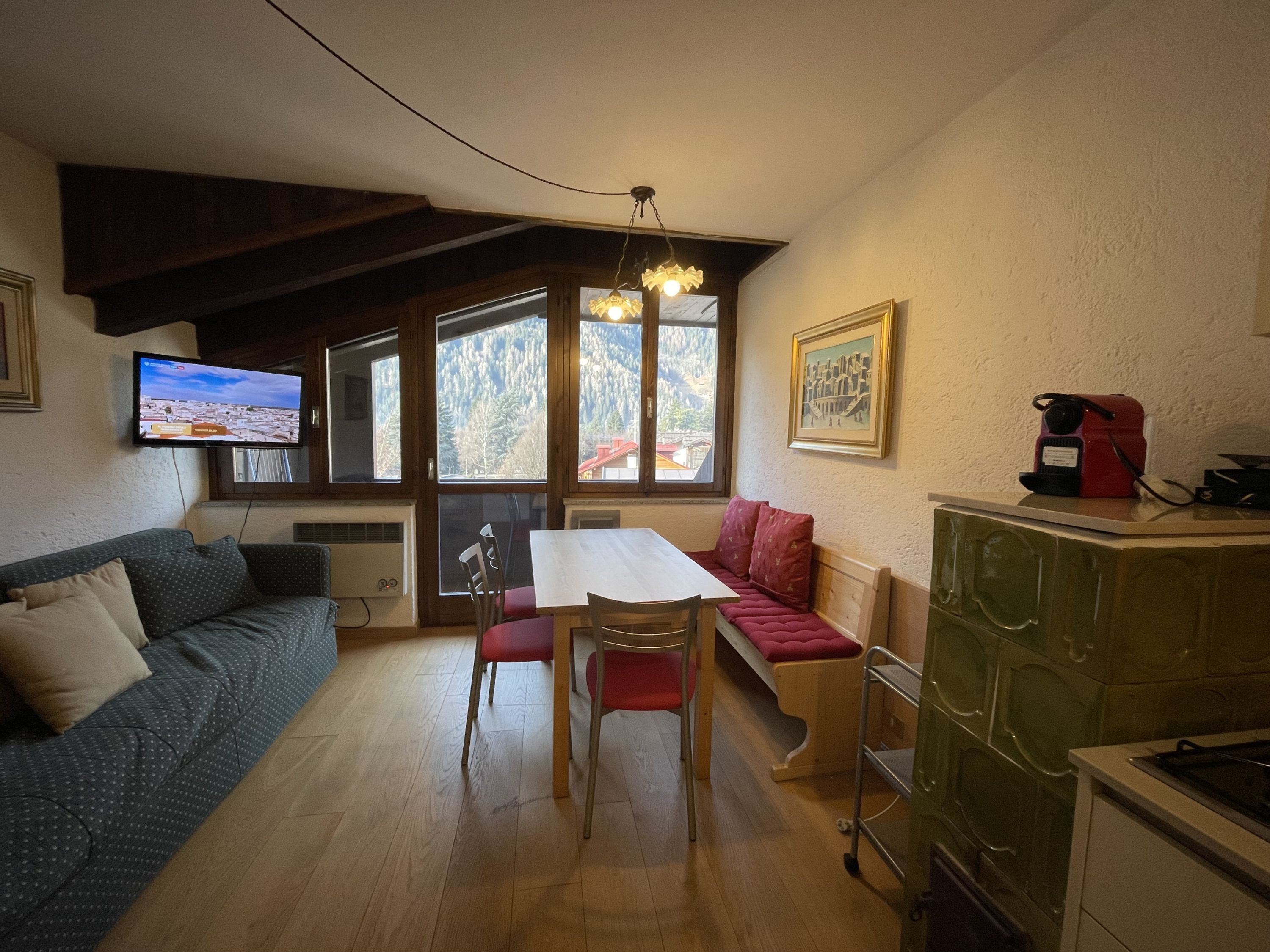 A cozy room with a wooden dining table, a sofa, a bench, and a TV mounted on the wall.
