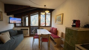 A cozy room with a wooden dining table, a sofa, a bench, and a TV mounted on the wall. - 079 Bilocale Pinzolo (Pinzolo)