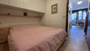 A bedroom with a bed, a dresser, a shelf with a lamp, and a framed picture on the wall. - 079 Bilocale Pinzolo (Pinzolo)
