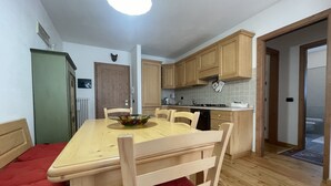 Een compacte keuken met houten kastjes, een eettafel met stoelen en een rode bank.