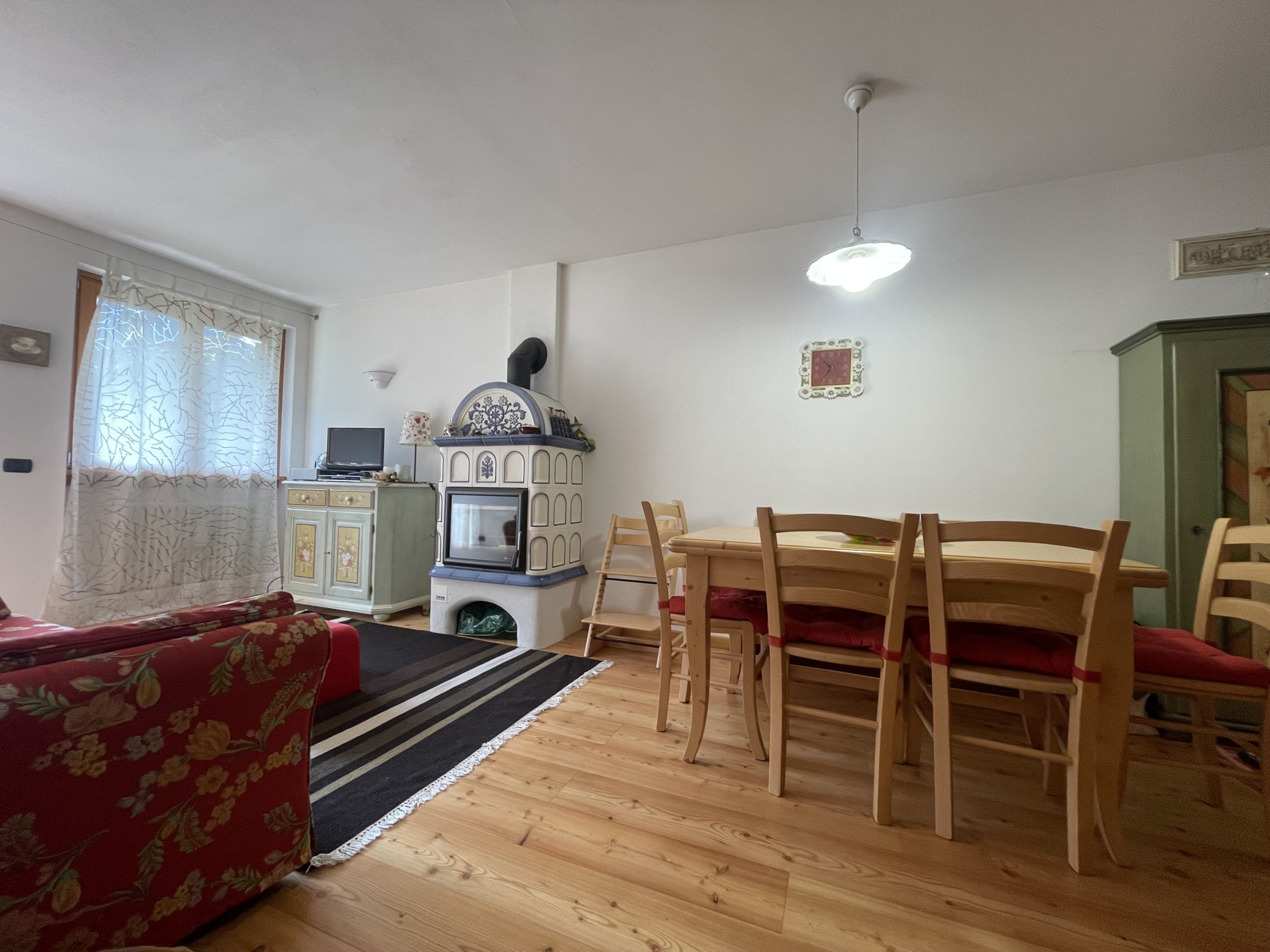 Een woonkamer met een houten tafel en stoelen, een bank, een decoratieve kachel en een raam met gordijnen.