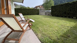 Een terras met twee loungestoelen, een verzorgd gazon, een houten omheining en een haag.