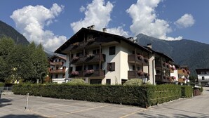 Ein mehrstöckiges Hotel mit Balkonen, einem Parkplatz und Bergen im Hintergrund.