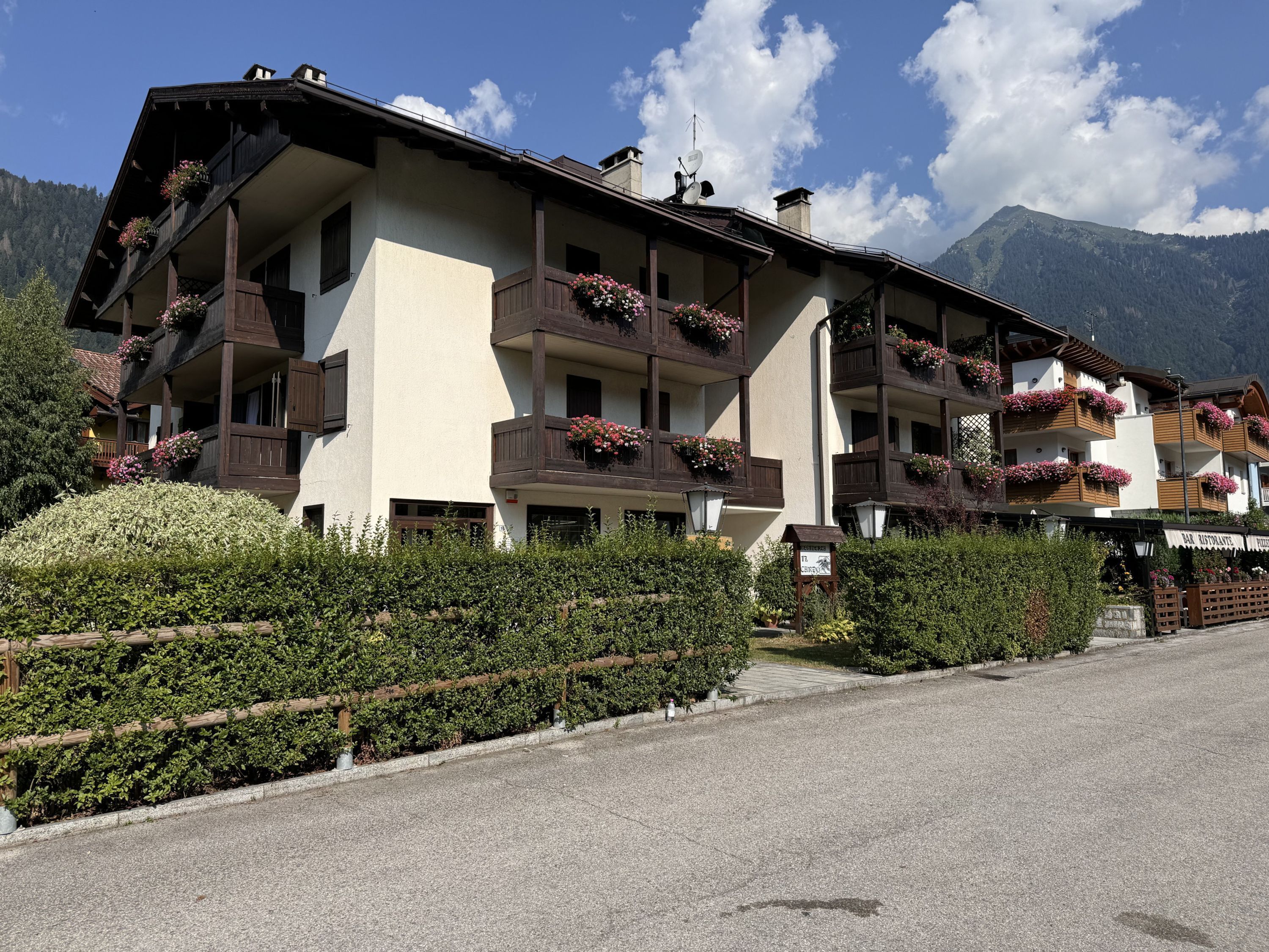 A multi-story hotel with balconies adorned with flowers, a sign for a restaurant, and a mountainous backdrop.