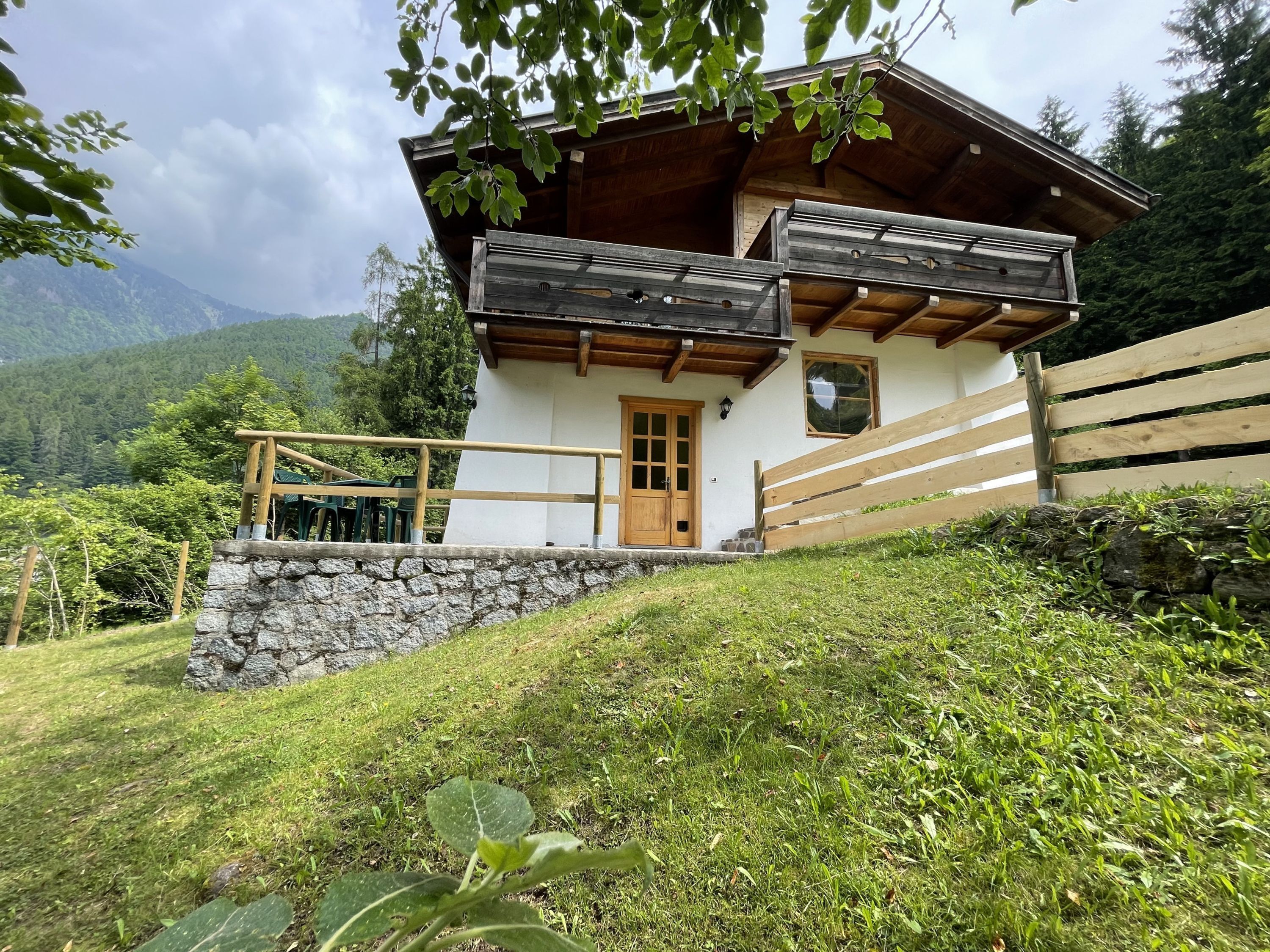 Een chalet met een stenen fundering, een houten balkon en uitzicht op de omliggende bergen.