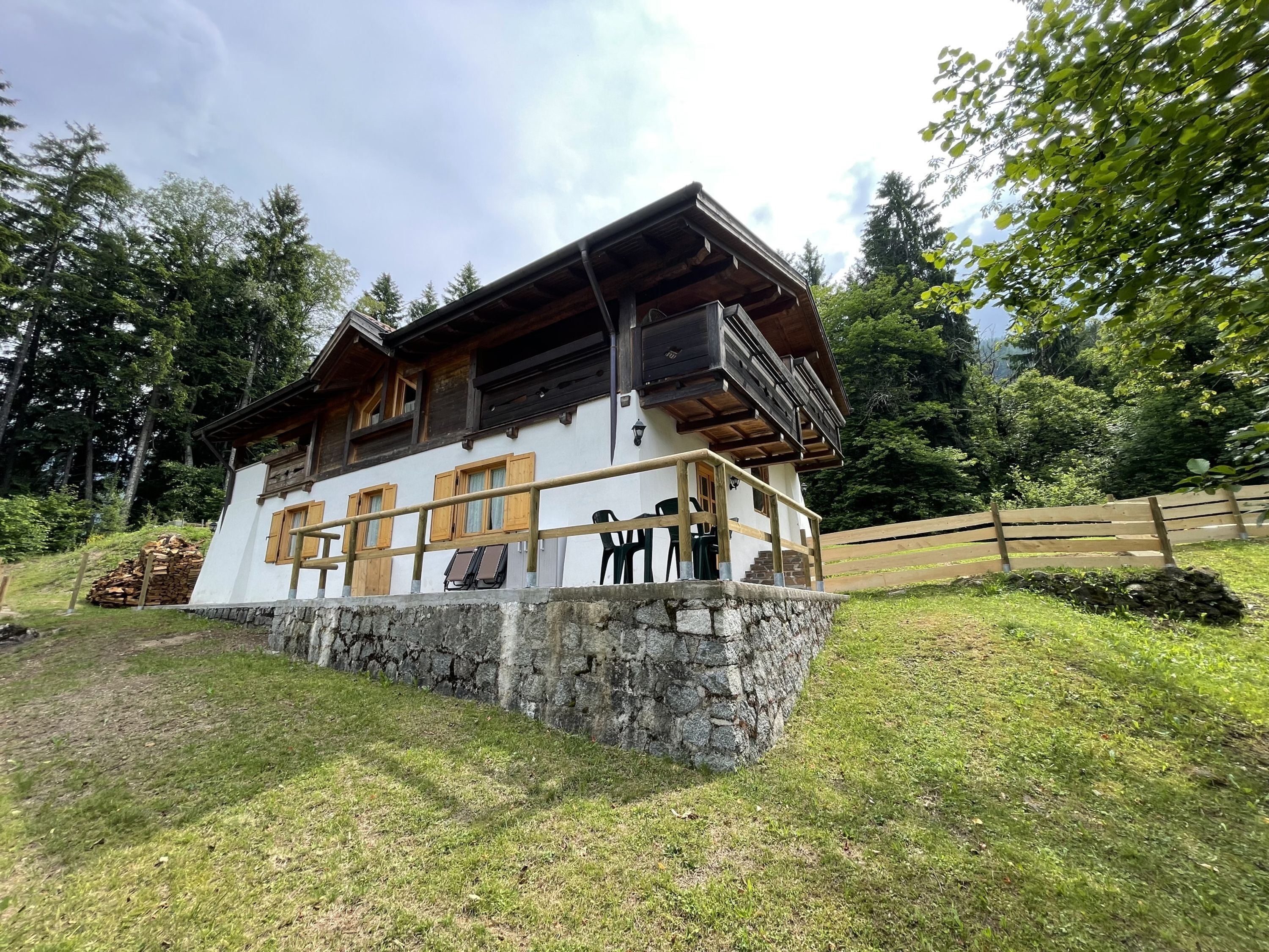 A chalet-style building with a stone foundation, wooden balcony, and multiple windows with shutters.