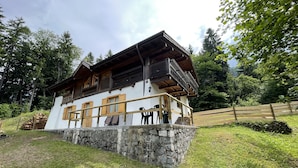 A chalet-style building with a stone foundation, wooden balcony, and multiple windows with shutters.