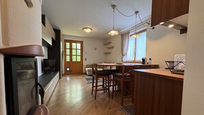 A compact kitchen with wooden cabinets, a dining area with a table and chairs, a built-in oven, and a window with curtains.