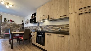 A modern kitchen with wooden cabinets, a black countertop, and a dining area with a table and chairs. - 082 Bilocale Pinzolo (Pinzolo)