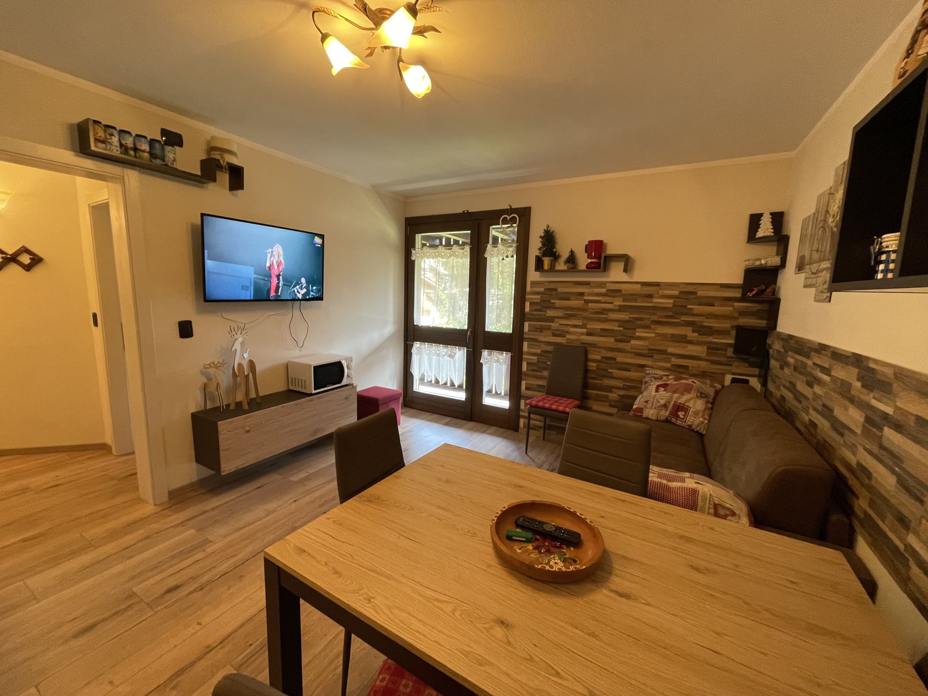 A modern living room with a wooden dining table, a television mounted on the wall, and a stone accent wall.