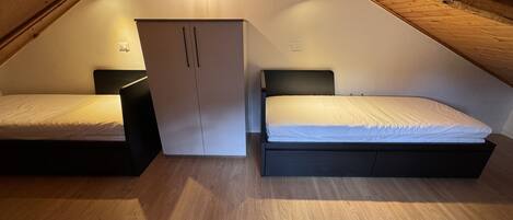 A small, triangular attic bedroom with two beds, a wardrobe, and a sloped ceiling.