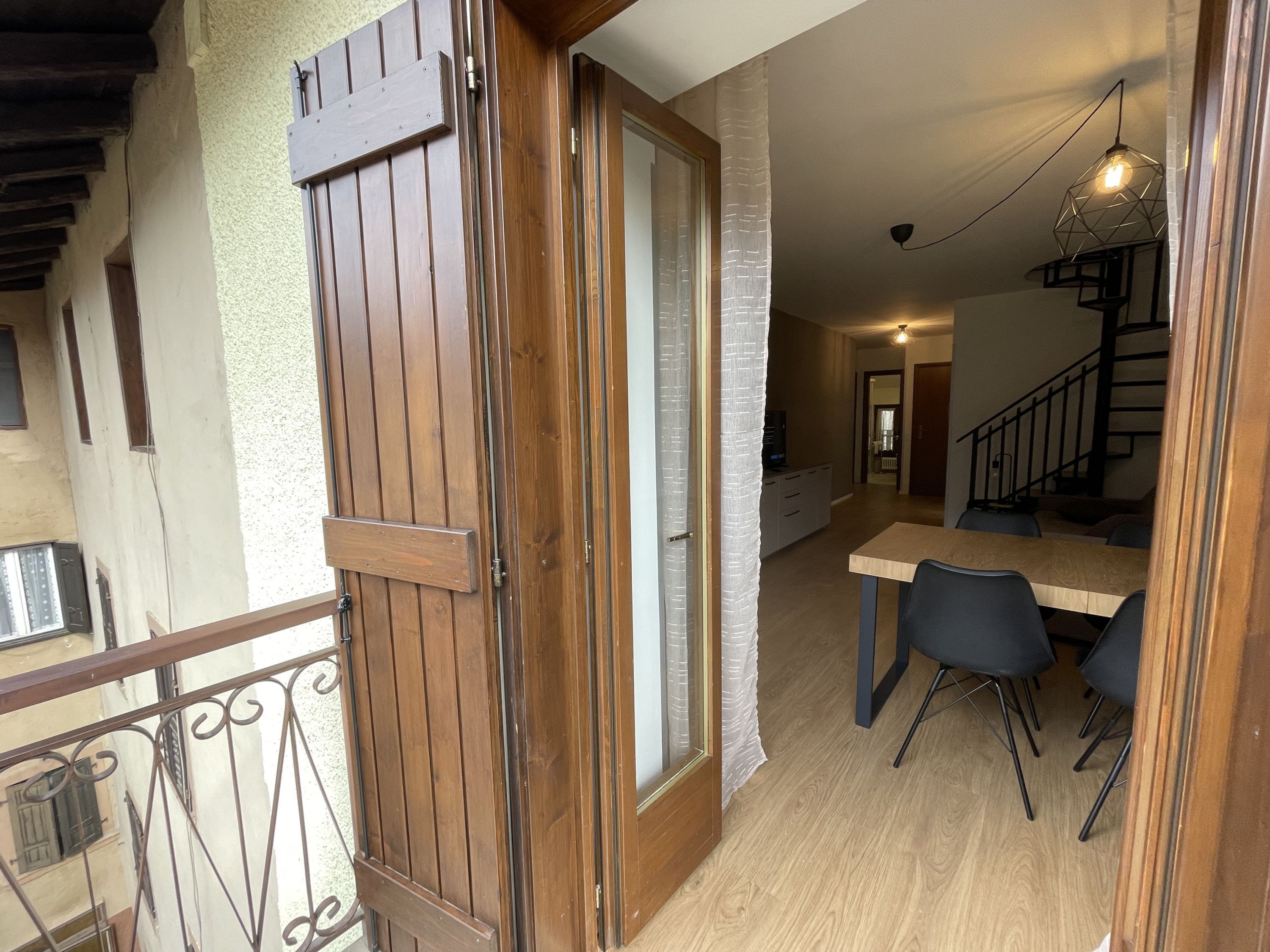 A wooden door leading into a room with a dining table and chairs, a staircase, and a hanging light fixture.